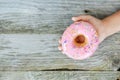ChildÃ¢â¬â¢s hand holding attractive pink doughnut on wooden table as background Royalty Free Stock Photo